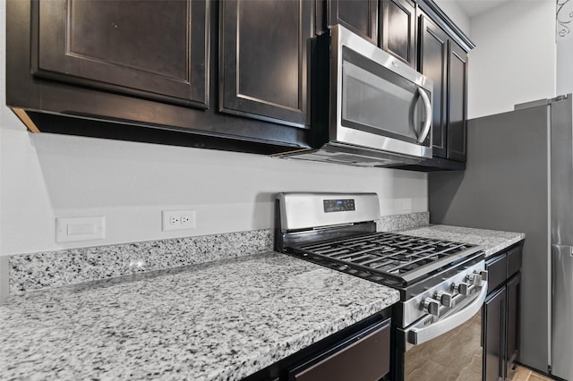 kitchen featuring appliances with stainless steel finishes, dark brown cabinets, light stone counters, and light wood-type flooring