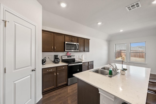 kitchen with a kitchen bar, sink, appliances with stainless steel finishes, light stone countertops, and a kitchen island with sink