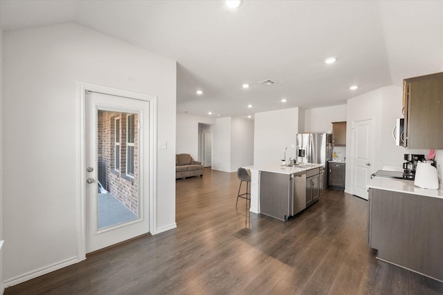 kitchen featuring an island with sink, lofted ceiling, a breakfast bar area, dark hardwood / wood-style flooring, and stainless steel appliances