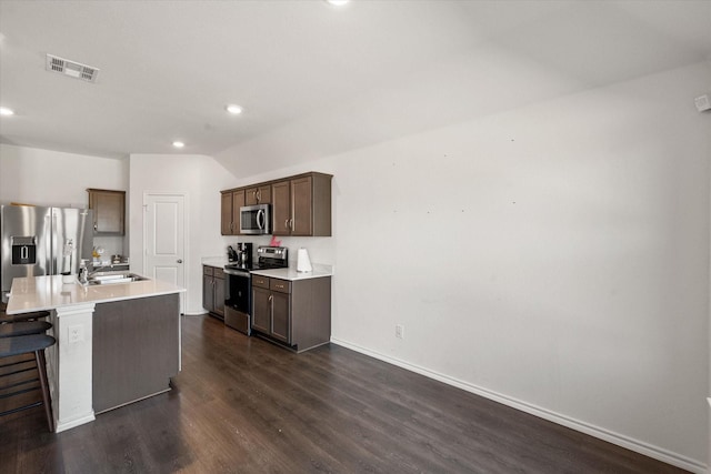 kitchen featuring appliances with stainless steel finishes, dark hardwood / wood-style floors, sink, a kitchen bar, and a center island with sink