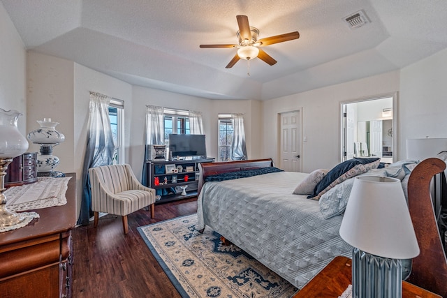 bedroom featuring dark hardwood / wood-style floors, ensuite bath, ceiling fan, a raised ceiling, and a textured ceiling