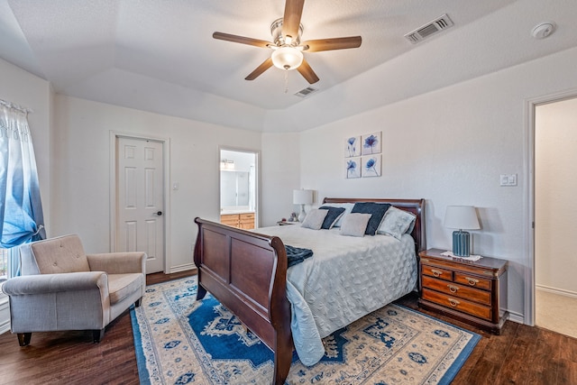 bedroom featuring multiple windows, dark hardwood / wood-style flooring, ceiling fan, a tray ceiling, and ensuite bath