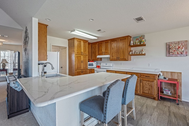 kitchen featuring sink, a textured ceiling, a kitchen breakfast bar, kitchen peninsula, and white appliances