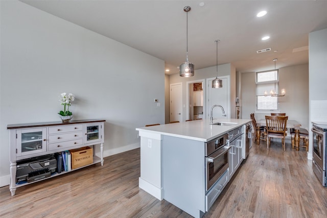 kitchen featuring sink, hardwood / wood-style flooring, a kitchen island with sink, stainless steel appliances, and decorative light fixtures