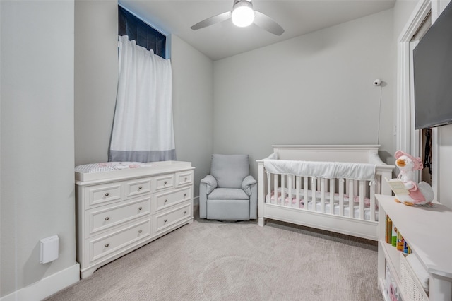 bedroom with a nursery area, ceiling fan, and light carpet