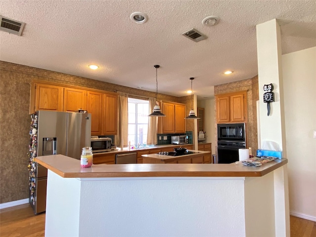 kitchen with pendant lighting, black appliances, kitchen peninsula, a textured ceiling, and light hardwood / wood-style flooring