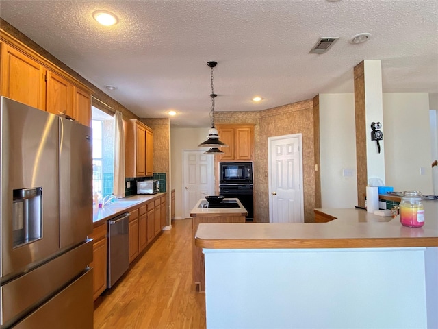 kitchen featuring kitchen peninsula, a kitchen island, pendant lighting, light hardwood / wood-style floors, and black appliances