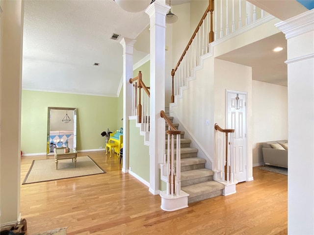 stairway featuring ornate columns, ornamental molding, a high ceiling, and hardwood / wood-style floors