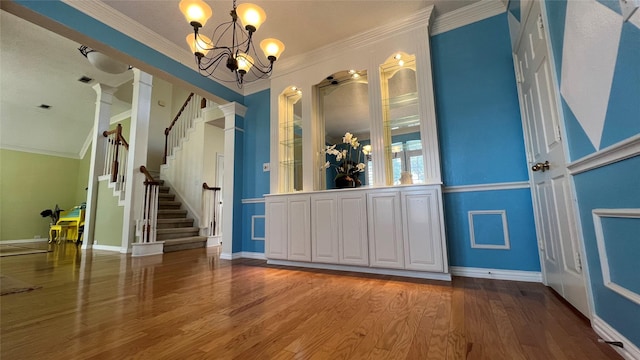 interior space with pendant lighting, hardwood / wood-style floors, decorative columns, ornamental molding, and a chandelier