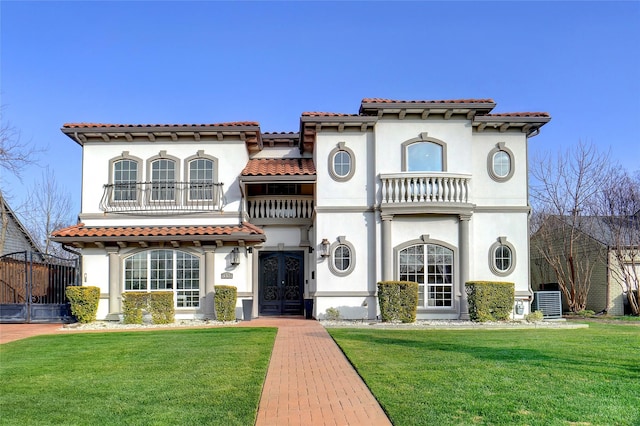 mediterranean / spanish-style home with french doors, a balcony, central AC unit, and a front lawn