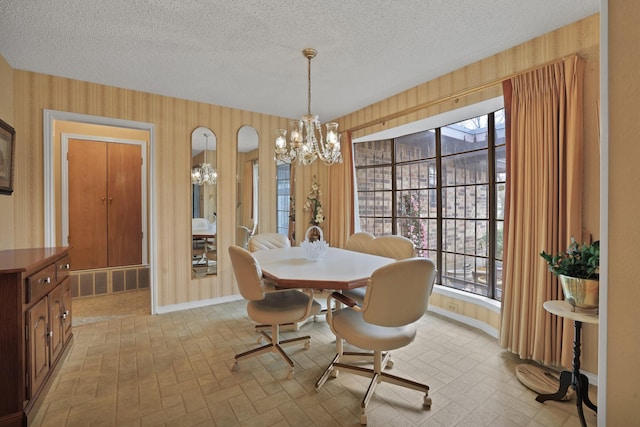 dining room with an inviting chandelier, a healthy amount of sunlight, wooden walls, and a textured ceiling