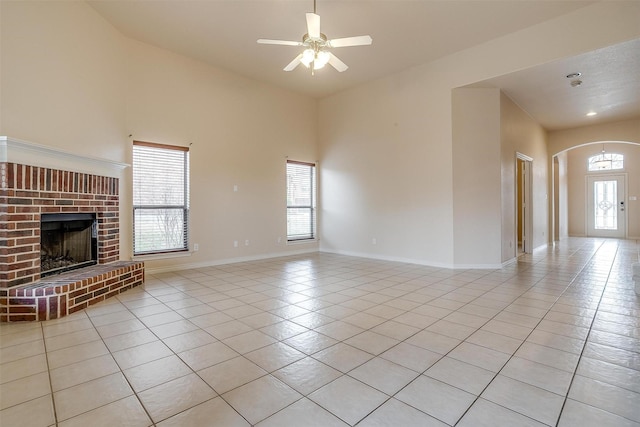 unfurnished living room with a brick fireplace, a healthy amount of sunlight, light tile patterned floors, and ceiling fan