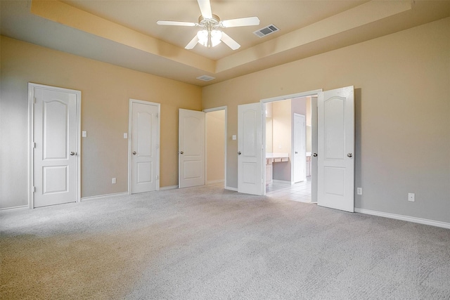 unfurnished bedroom featuring ceiling fan, a raised ceiling, and light carpet