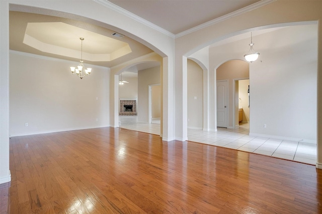 unfurnished living room with a raised ceiling, ornamental molding, a fireplace, and light hardwood / wood-style flooring