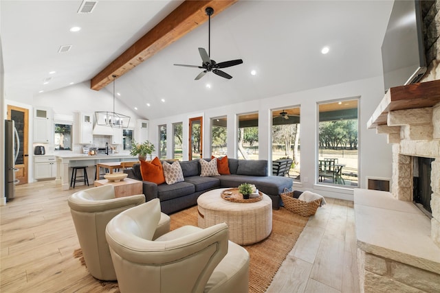 living room featuring a stone fireplace, ceiling fan with notable chandelier, high vaulted ceiling, beamed ceiling, and light hardwood / wood-style floors