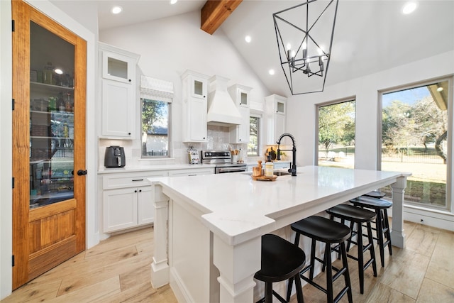 kitchen with sink, custom exhaust hood, white cabinetry, a center island with sink, and stainless steel electric stove