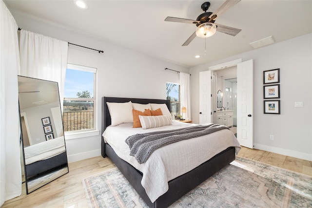 bedroom featuring multiple windows, ensuite bathroom, ceiling fan, and light wood-type flooring