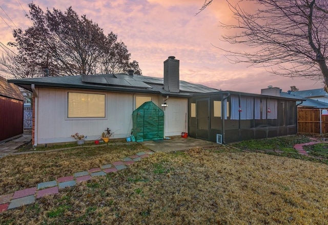 back house at dusk featuring a sunroom, a lawn, and solar panels