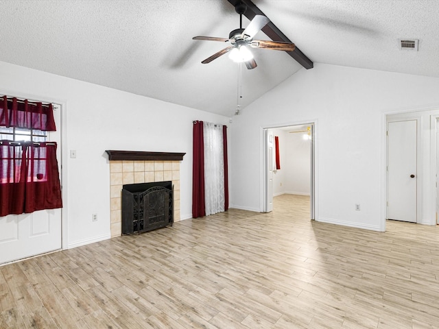 unfurnished living room featuring lofted ceiling with beams, a tiled fireplace, ceiling fan, a textured ceiling, and light hardwood / wood-style flooring