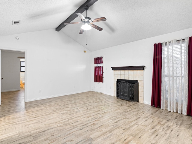 unfurnished living room featuring a tile fireplace, vaulted ceiling with beams, light wood-type flooring, ceiling fan, and a textured ceiling