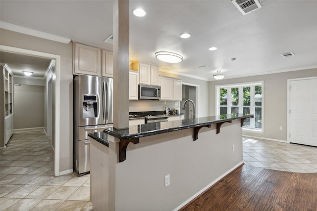 kitchen featuring a breakfast bar area, crown molding, dark stone countertops, stainless steel appliances, and a kitchen island with sink