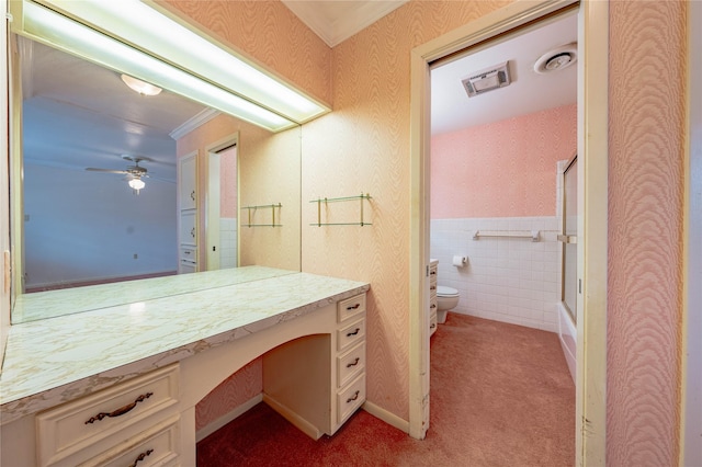 full bath featuring toilet, tile walls, vanity, wainscoting, and wallpapered walls