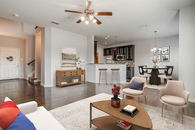 living room featuring ceiling fan with notable chandelier and dark wood-type flooring