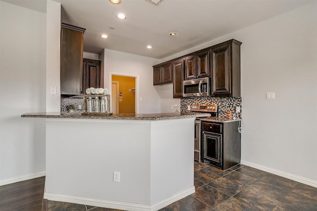 kitchen with dark brown cabinetry, appliances with stainless steel finishes, kitchen peninsula, dark stone counters, and backsplash