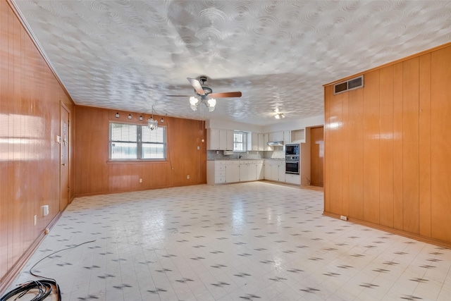 unfurnished living room featuring wooden walls and ceiling fan