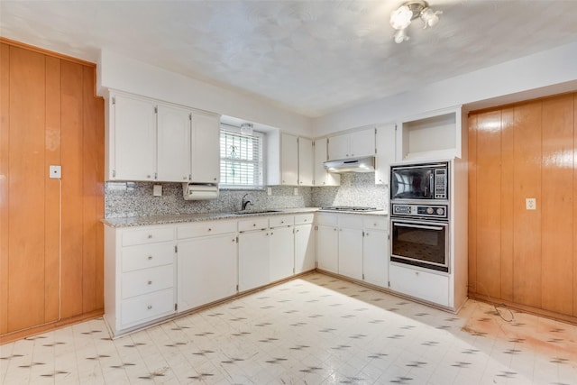 kitchen featuring sink, black oven, white cabinetry, built in microwave, and wood walls