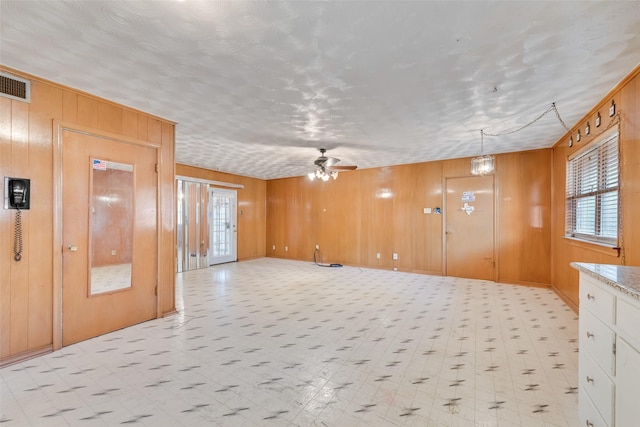 unfurnished room featuring ceiling fan with notable chandelier and wood walls