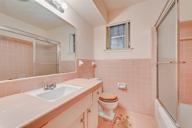 full bathroom featuring combined bath / shower with glass door, tile walls, tile patterned flooring, vanity, and toilet