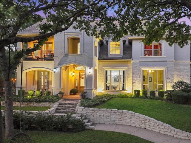 view of front of home featuring a front lawn, a balcony, french doors, and brick siding