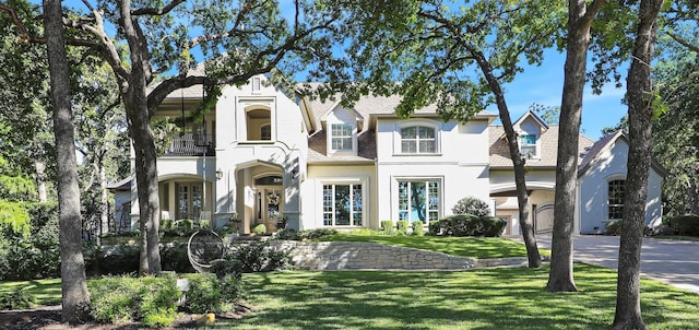 view of front of house featuring stucco siding, a front yard, a balcony, and driveway