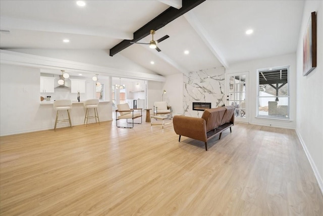 living room featuring ceiling fan, a fireplace, light hardwood / wood-style flooring, and vaulted ceiling with beams