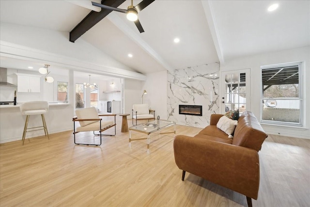 living room with lofted ceiling with beams, light wood-type flooring, ceiling fan with notable chandelier, and a high end fireplace