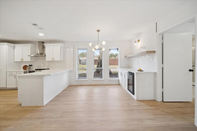 kitchen with wine cooler, white cabinets, decorative light fixtures, kitchen peninsula, and wall chimney exhaust hood