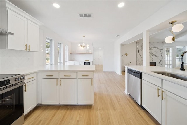 kitchen with pendant lighting, sink, white cabinets, stainless steel appliances, and wall chimney exhaust hood