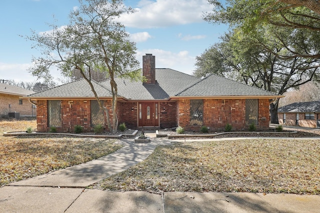 single story home with brick siding, a chimney, central AC unit, and a shingled roof