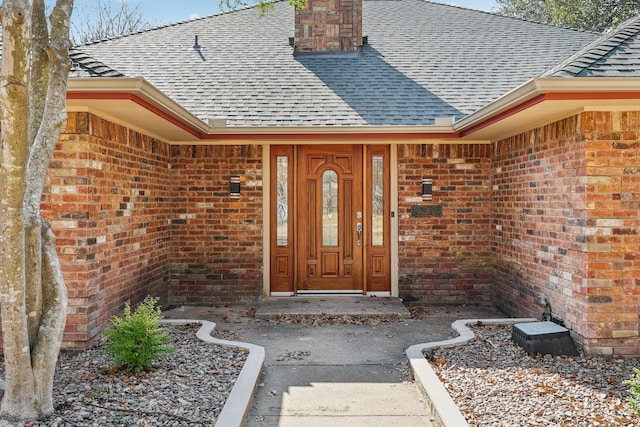 doorway to property with brick siding, a chimney, and roof with shingles