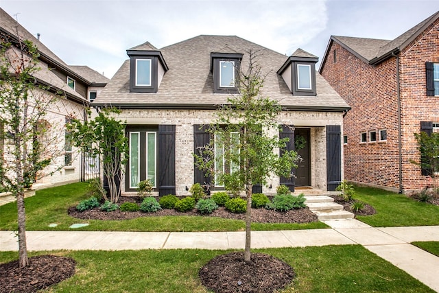 view of front of home featuring a shingled roof, a front lawn, and brick siding