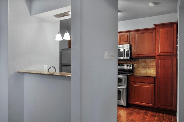 kitchen with dark wood-type flooring, light stone counters, tasteful backsplash, hanging light fixtures, and appliances with stainless steel finishes