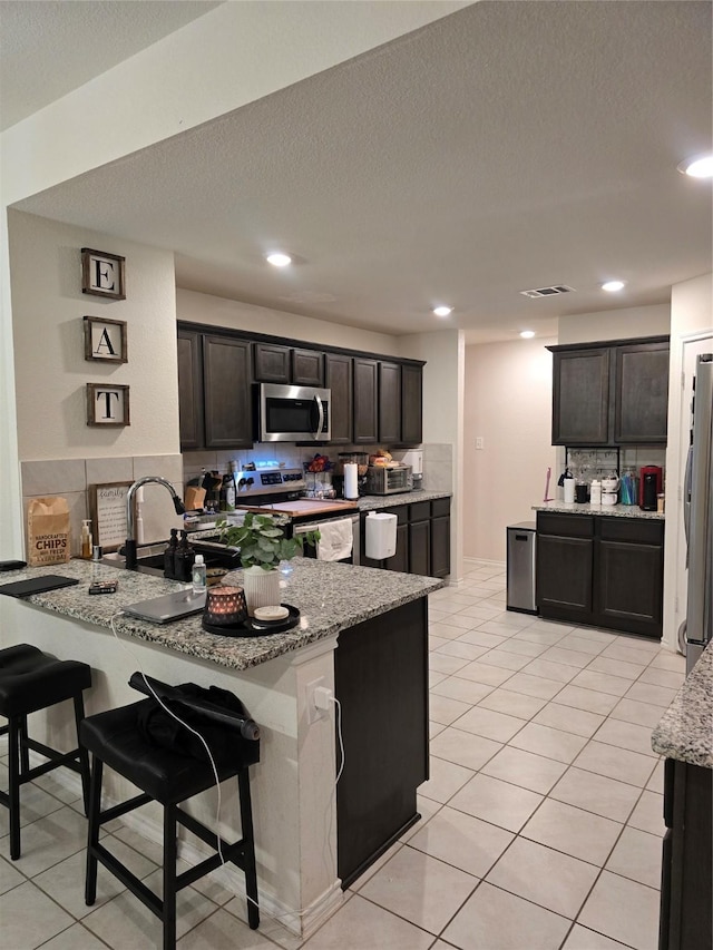 kitchen featuring stainless steel appliances, a kitchen breakfast bar, kitchen peninsula, and light stone countertops