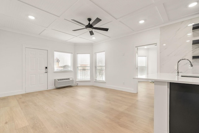 unfurnished living room featuring sink, ceiling fan, a wall mounted AC, coffered ceiling, and light wood-type flooring