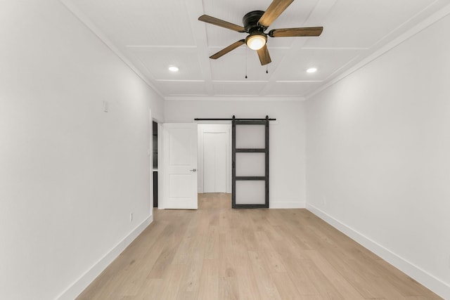 unfurnished bedroom featuring coffered ceiling, light wood-type flooring, ornamental molding, ceiling fan, and a barn door