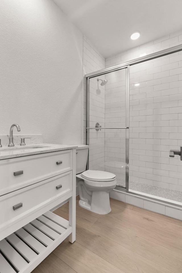 bathroom featuring hardwood / wood-style flooring, vanity, a shower with door, and toilet