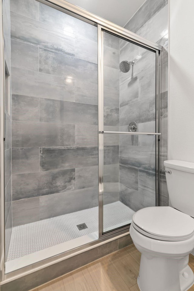 bathroom featuring a shower with door, hardwood / wood-style floors, and toilet