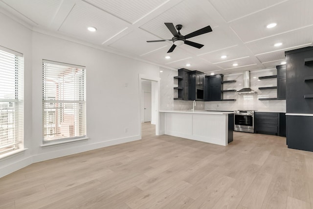 kitchen with wall chimney range hood, ceiling fan, backsplash, stainless steel range oven, and light wood-type flooring