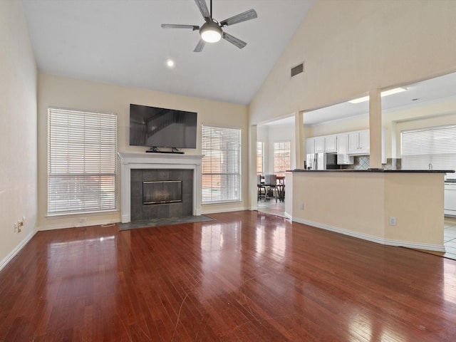 unfurnished living room featuring high vaulted ceiling, hardwood / wood-style flooring, a tile fireplace, and ceiling fan