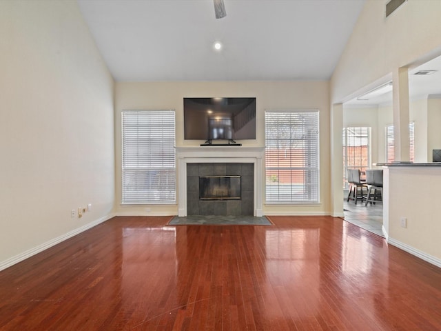 unfurnished living room featuring a tile fireplace, vaulted ceiling, and wood-type flooring